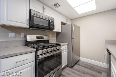 Kitchen featuring stainless steel appliances, white cabinetry, light wood-style floors, and light stone countertops
