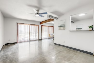 Unfurnished room featuring concrete flooring, beamed ceiling, and a ceiling fan