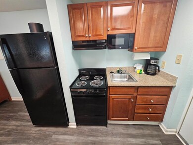 Kitchen featuring black appliances, under cabinet range hood, dark wood-type flooring, and brown cabinets