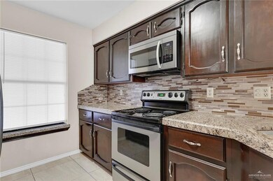 Kitchen with stainless steel appliances, dark brown cabinets, backsplash, light tile patterned floors, and light stone counters