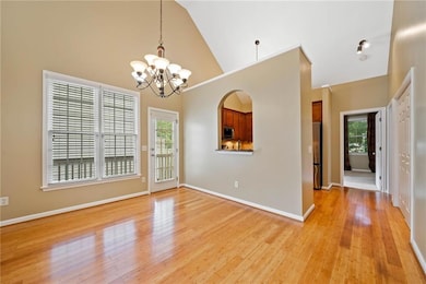 Empty room featuring a chandelier, high vaulted ceiling, healthy amount of natural light, light wood finished floors, and baseboards