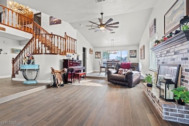 Living room with a brick fireplace, high vaulted ceiling, wood finished floors, a ceiling fan, and stairway