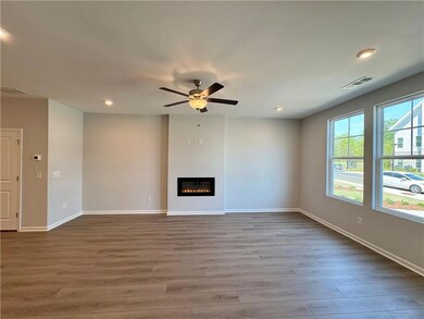 Unfurnished living room featuring a glass covered fireplace, baseboards, visible vents, ceiling fan, and wood finished floors