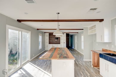 Kitchen with white cabinetry, light wood-style floors, beamed ceiling, decorative light fixtures, and wood counters