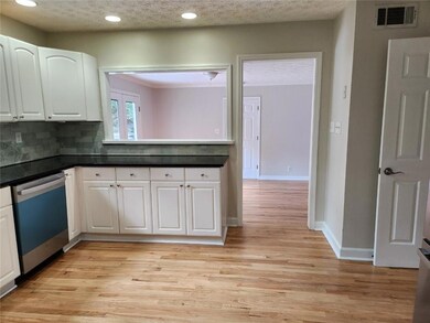 Kitchen with dishwashing machine, white cabinets, dark countertops, light wood-type flooring, and recessed lighting
