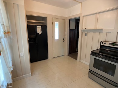 Kitchen with stainless steel range with electric stovetop, white cabinetry, black refrigerator with ice dispenser, and light tile flooring