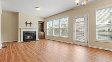 Unfurnished living room featuring light wood-style flooring, a fireplace with flush hearth, built in shelves, and a chandelier