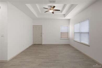 Empty room with a tray ceiling, ceiling fan, and light wood-type flooring