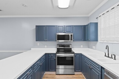 Kitchen with blue cabinets, appliances with stainless steel finishes, crown molding, light countertops, and light wood-type flooring