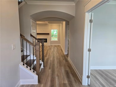 Hall featuring arched walkways, wood finished floors, stairway, baseboards, and crown molding