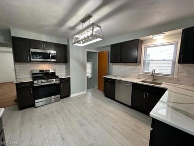 Kitchen featuring backsplash, quartz countertops, appliances with stainless steel finishes, ceramic flooring, and cabinetry