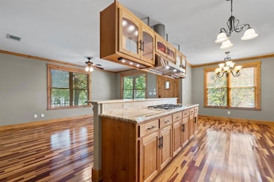 Kitchen featuring ornamental molding, hanging light fixtures, glass insert cabinets, light wood-style flooring, and a center island