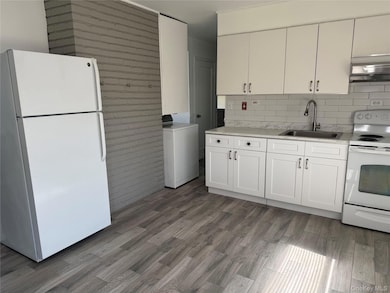 Kitchen with white appliances, white cabinets, washer / dryer, light wood-style floors, and tasteful backsplash