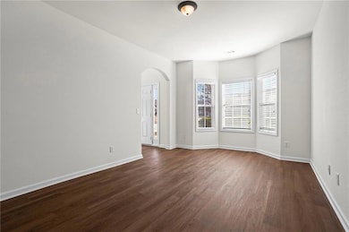 Empty room featuring arched walkways, dark wood-style flooring, and baseboards