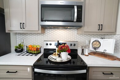 Kitchen with electric range oven, stainless steel microwave, decorative backsplash, and light stone counters