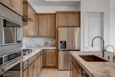Kitchen with stainless steel appliances, backsplash, light tile patterned flooring, a sink, and light stone countertops