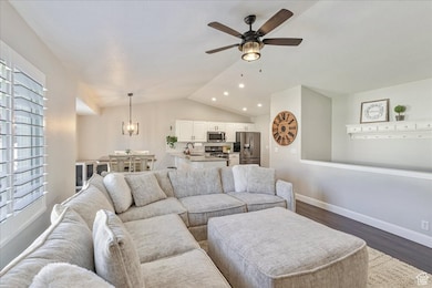 Living room with lofted ceiling, dark wood-style floors, a ceiling fan, a chandelier, and recessed lighting