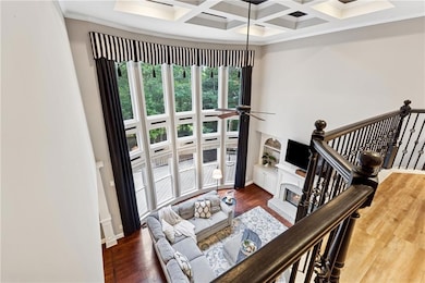 Living room featuring beam ceiling, ornamental molding, wood finished floors, coffered ceiling, and a brick fireplace