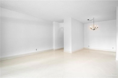 Empty room featuring a chandelier, a textured ceiling, and baseboards
