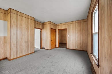 Unfurnished bedroom featuring light carpet, wood walls, and baseboard heating