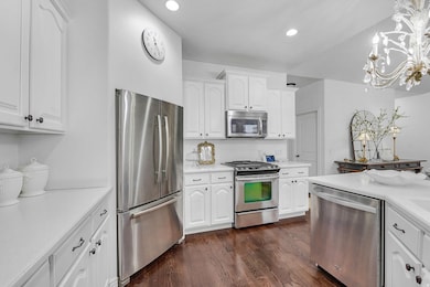 Kitchen with white cabinetry, appliances with stainless steel finishes, dark wood-style flooring, hanging light fixtures, and recessed lighting