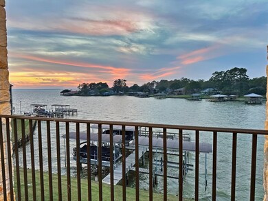 This photo showcases a serene waterfront view from a balcony, featuring a dock and boathouse on a calm body of water, with a stunning sunset and lush greenery in the background. Ideal for those seeking a tranquil lakeside retreat.