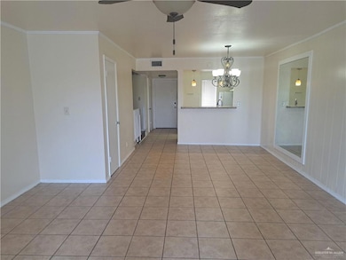 Unfurnished room featuring ceiling fan with notable chandelier, baseboards, light tile patterned floors, visible vents, and ornamental molding