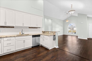 Kitchen featuring white cabinetry, a peninsula, dark wood finished floors, backsplash, and high vaulted ceiling