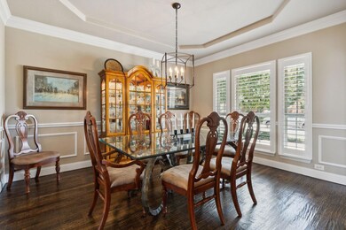 Dining space with dark wood-type flooring, a chandelier, a tray ceiling, and ornamental molding