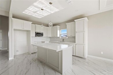 Kitchen featuring stainless steel microwave, light marble finish flooring, a kitchen island, white cabinetry, and baseboards