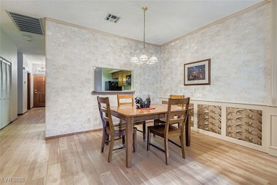 Dining area featuring a textured ceiling, a chandelier, light wood-style flooring, wallpapered walls, and ornamental molding