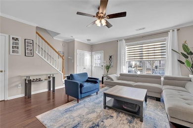 Living area with ceiling fan, wood finished floors, stairway, ornamental molding, and baseboards