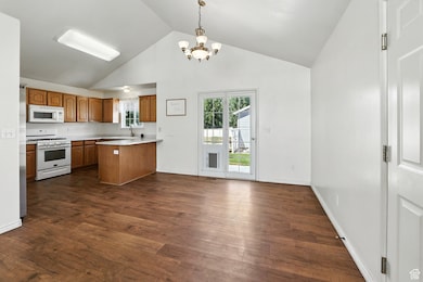 Kitchen with brown cabinetry, a peninsula, white appliances, light countertops, and high vaulted ceiling