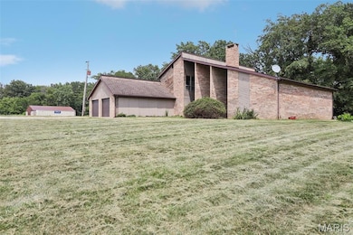 Back of property with a chimney, an attached garage, brick siding, and a yard