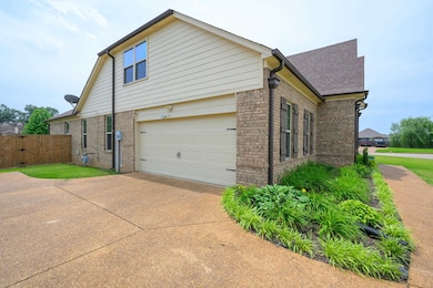 View of side of property featuring brick siding, fence, driveway, roof with shingles, and a garage