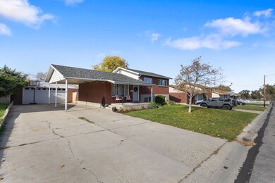 Tri-level home with a porch, brick siding, concrete driveway, an outdoor structure, and a front yard