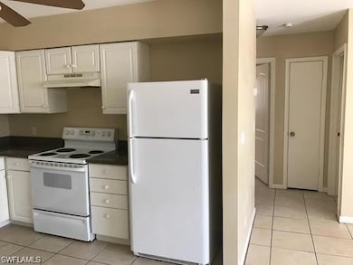 Kitchen with white appliances, under cabinet range hood, light tile patterned floors, and dark countertops