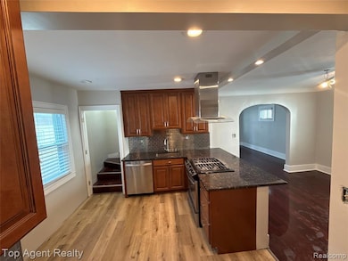 Kitchen featuring dark stone counters, stainless steel appliances, island range hood, decorative backsplash, and light wood-type flooring