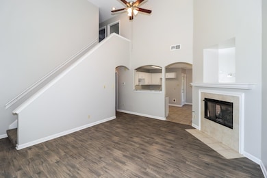 Unfurnished living room featuring a towering ceiling, arched walkways, dark wood finished floors, a tiled fireplace, and ceiling fan
