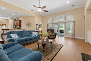 Living area with arched walkways, light wood-style floors, a ceiling fan, crown molding, and baseboards