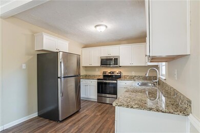 Kitchen featuring dark hardwood / wood-style floors, sink, white cabinetry, light stone countertops, and stainless steel appliances