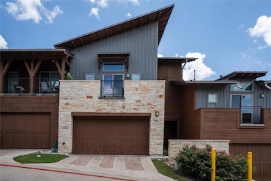 Contemporary house with stone siding, a balcony, a garage, and driveway