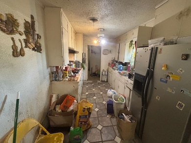 Kitchen with stainless steel fridge, light countertops, a textured ceiling, white cabinetry, and a textured wall