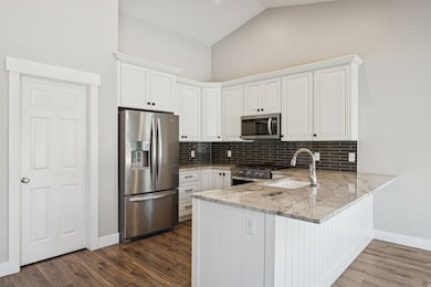 Kitchen with appliances with stainless steel finishes, light stone countertops, a peninsula, white cabinets, and high vaulted ceiling