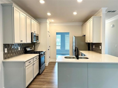 Kitchen featuring appliances with stainless steel finishes, crown molding, decorative backsplash, dark wood finished floors, and a peninsula