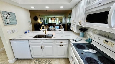 Kitchen featuring white appliances, a sink, a chandelier, white cabinets, and recessed lighting