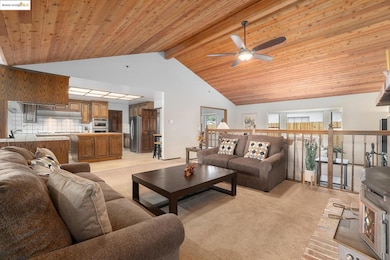 Living room featuring light colored carpet, high vaulted ceiling, a wooden ceiling with exposed beams, a wood stove, and a ceiling fan