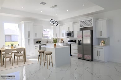 Kitchen featuring a tray ceiling, appliances with stainless steel finishes, decorative light fixtures, a center island, and light marble finish floors