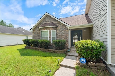 Doorway to property featuring a lawn, stone siding, and roof with shingles