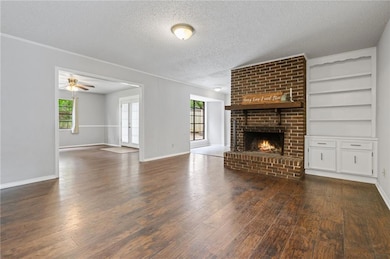 Unfurnished living room featuring dark wood-type flooring, a textured ceiling, a brick fireplace, baseboards, and built in features
